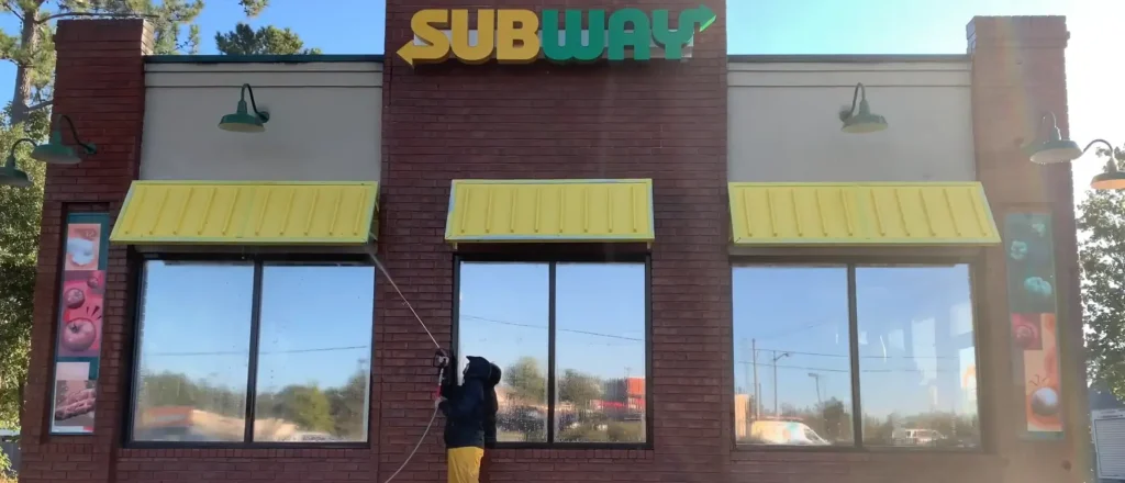 Technician pressure washing the brick exterior and windows of a commercial building in Jacksonville, FL